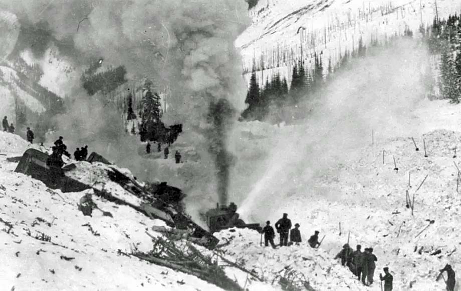 A rotary snow plow and men clear the track in Rogers Pass.